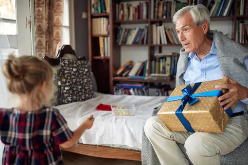 дедушка сидит на кровати с подарком от внучки