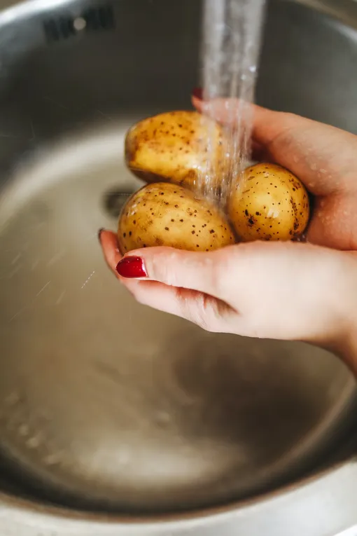 Руки держат картошку под струёй воды