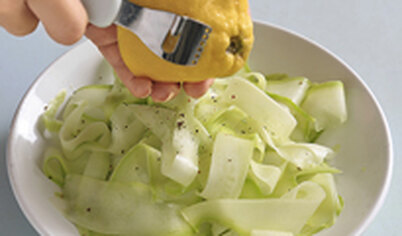 Ленты кабачков выложите в отдельную емкость, присыпьте солью и перцем, добавьте лимонную цедру, а также лимонный сок и 2 ст. л. оливкового масла.