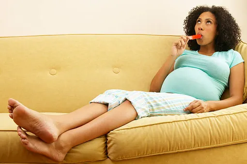 темнокожая беременная женщина лежит на диване и сосет леденец