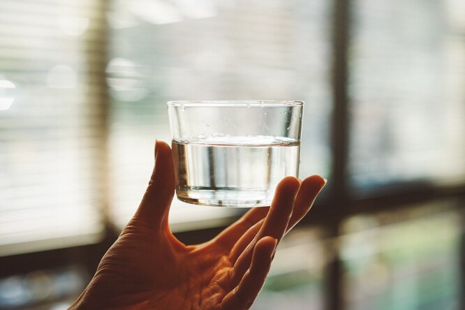 Рука держит стакан с водой, сколько нужно пить воды в сутки