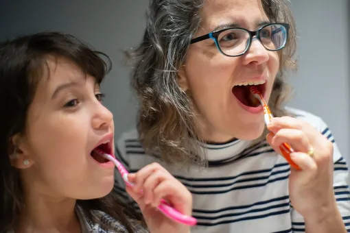 Мама с дочкой чистят зубы цветными щетками