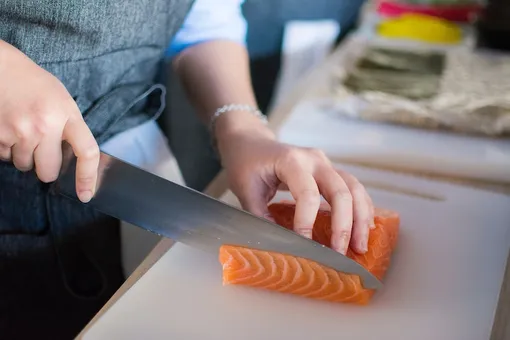 Рука режет ножом красную рыбу