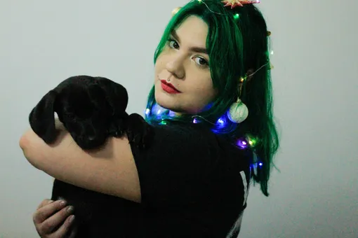 Женщина в новогодних игрушках с чёрной собакой на руках фото