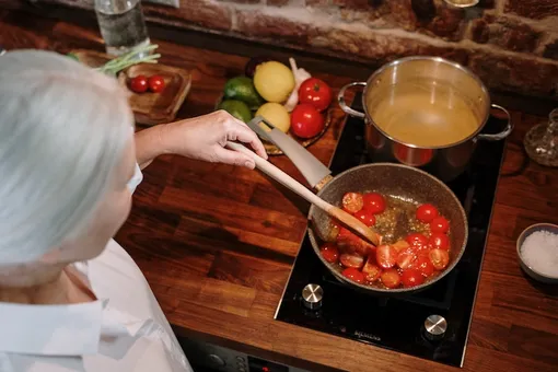 Седая женщина готовит на сковородки помидоры черри