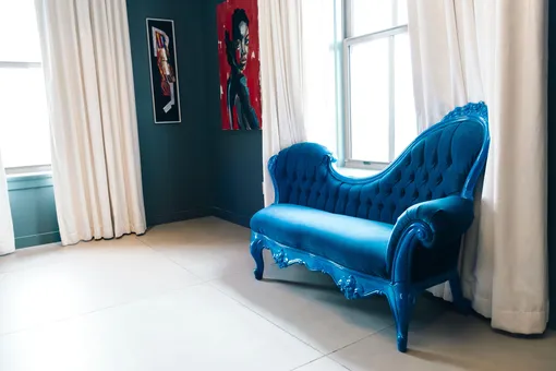 Винтажный викторианский диван королевского синего цвета в светлой комнате с большими окнами, картинами и белыми шторами