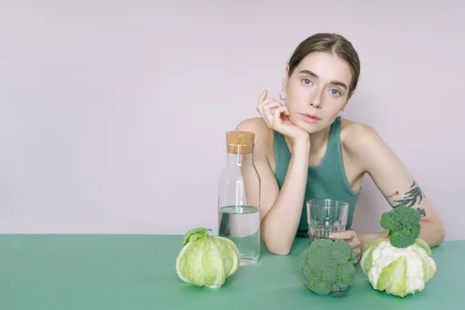 девушка сидит за столом с водой и овощами