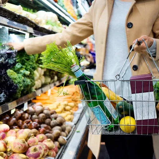 Девушка в супермаркете держит корзинку с овощами и зеленью