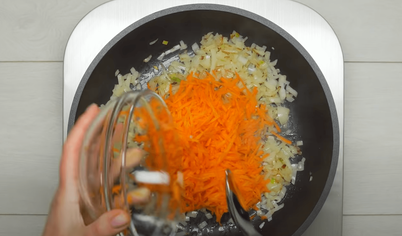 Налейте в сковородку растительное масло, положите лук и морковь, обжаривайте 5 минут, помешивая.