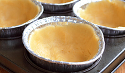Выложите тесто в смазанные маслом формочки, распределите по дну и бортикам. Поставьте их в большую форму с выемками для кексов, выпекайте 10–15 минут в духовке, нагретой до 200 градусов. Выньте, дайте остыть.