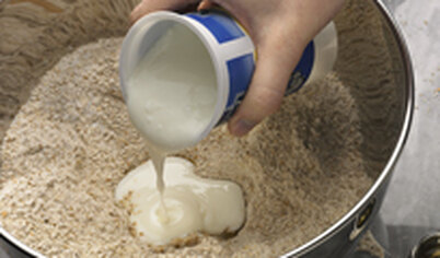 Сделайте в центре углубление и влейте пахту (кефир). Смешайте ложкой, добавляя по необходимости молоко. Вымесите гладкое тесто руками.
