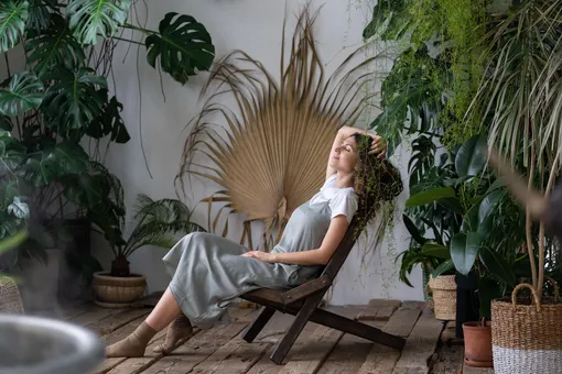 Девушка отдыхает на деревянном кресле среди комнатных растений