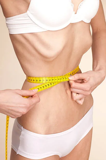 торс истощенной женщины с анорексией, она сантиметром измеряет талию