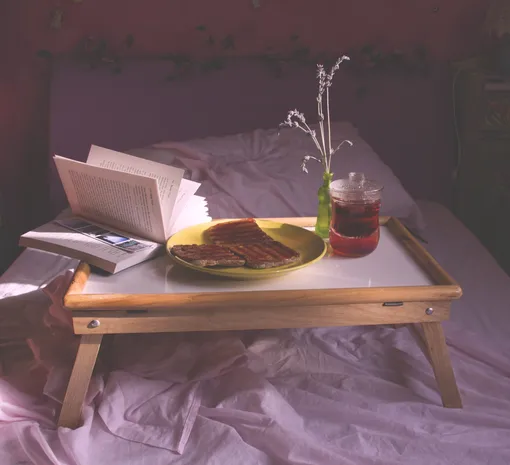 на кровати стоит столик с завтраком и книгой