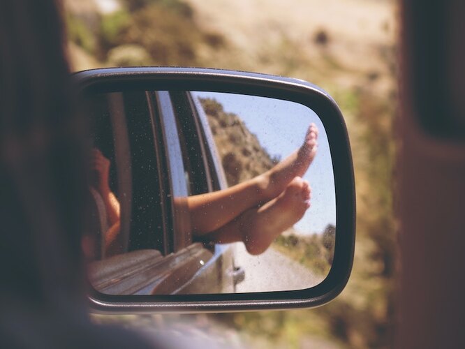 Ноги из окна машины, отражающиеся в зеркале