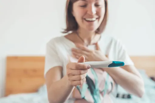 Женщина держит тест на беременность и улыбается