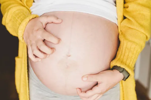 обнаженный беременный живот, женщина чешетего двумя руками