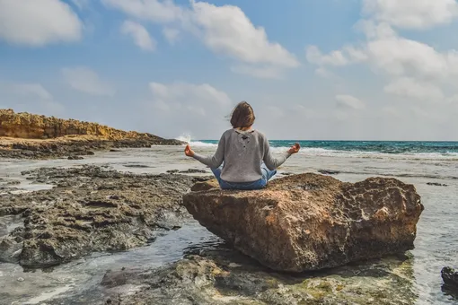 женщина медитирует на камнях рядом с морем