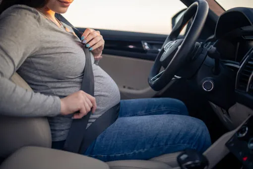 беременная женщина в машине, пристегнутая, за рулем