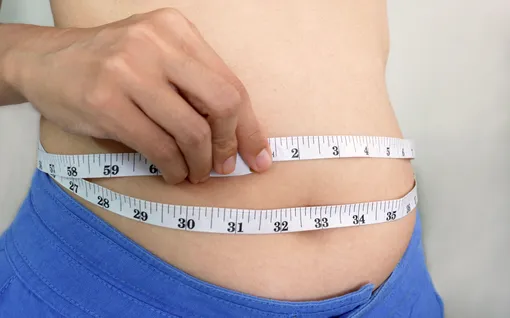 Женщина измеряет живот сантиметровой лентой