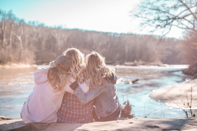 Три девушки сидят около реки на природе