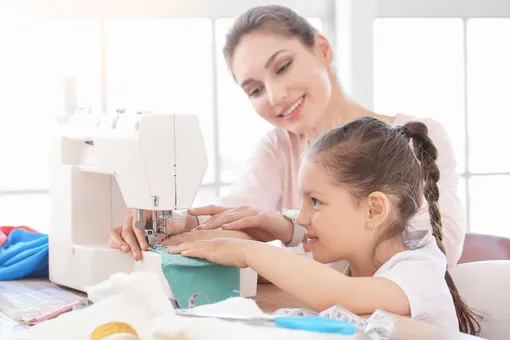 мама учит дочь шить на швейной машинке