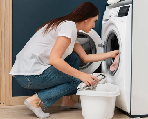 Девушка кладёт грязное бельё в стиральную машину