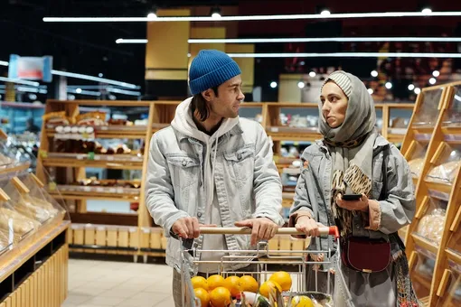 Пара смотрит друг на друга в супермаркете с тележкой с апельсинами