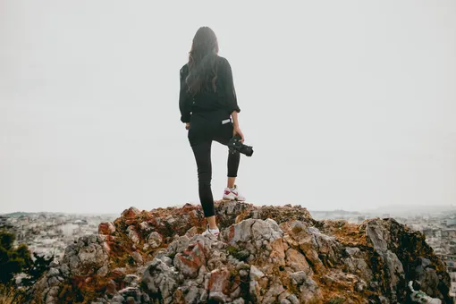 Девушка стоит на холме с фотоаппаратом в руках