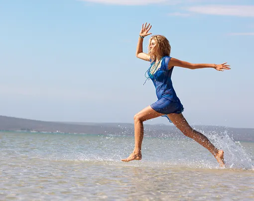 Женщина в синем бежит по морской воде
