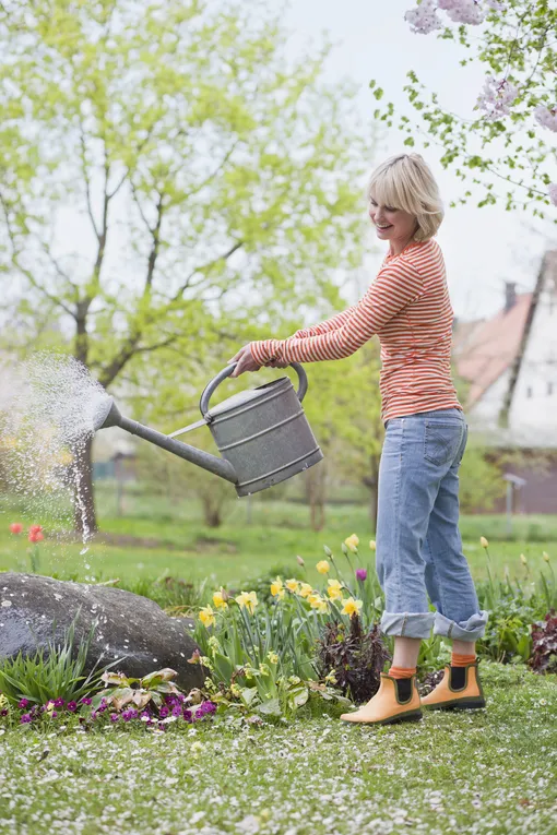 Женщина поливает растения, поливать днём в жару