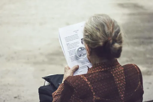 Женщина со спины читает газету с лупой