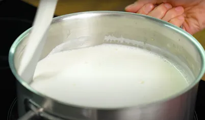 Параллельно приступайте к приготовлению крема для торта «Наполеон». Соедините в кастрюле муку, оба вида сахара и яйца. Тщательно перемешайте смесь венчиком и постепенно вливайте тёплое молоко, не переставая вымешивать. Должна получиться однородная масса.
Поставьте кастрюлю на небольшой огонь. Непрерывно помешивайте и следите, чтобы крем на начал липнуть ко дну. Как только он загустеет и начнёт побулькивать, снимайте.
