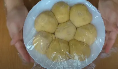 Разделите тесто для медовика на восемь частей и сформируйте шарики. Посыпьте мукой, выложите на терелку и накройте пищевой плёнкой. Отправьте в холодильник.
