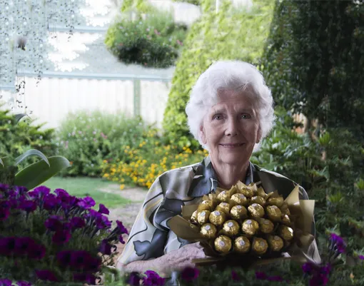 бабушка в саду держит в руках букет из конфет