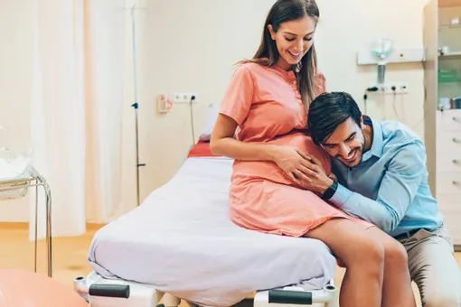 беременная женщина сидит на больничной кушетке, мужчина прижался щекой к ее животу