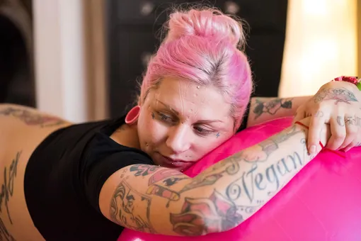 Беременная женщина с татуировками, пирсингом и розовыми волосами рожает