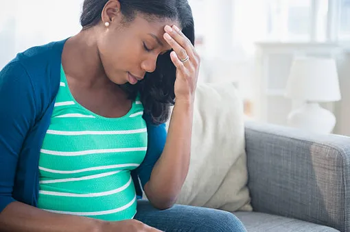 темнокожая беременная женщина сидит на диване и держится за голову