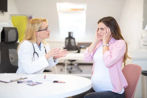 беременная женщина в кабинете у врача держится за голову