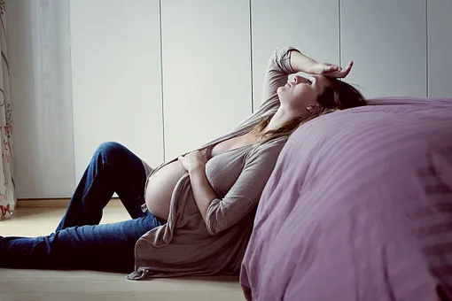 уставшая беременная женщина лежит на кровати, одна рука на лбу, другая на животе