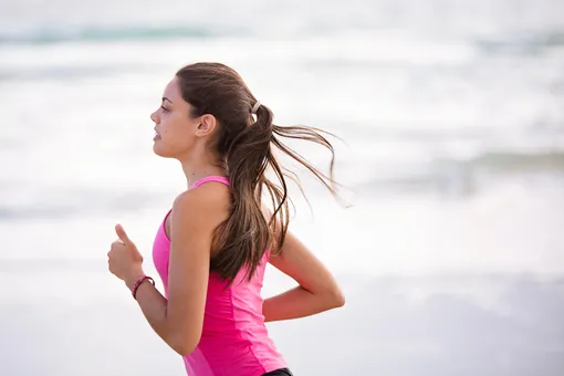 Женщина занимается фитнесом, бежит вдоль моря