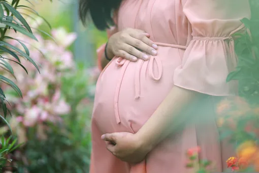 беременная девушка стоит в саду среди цветов