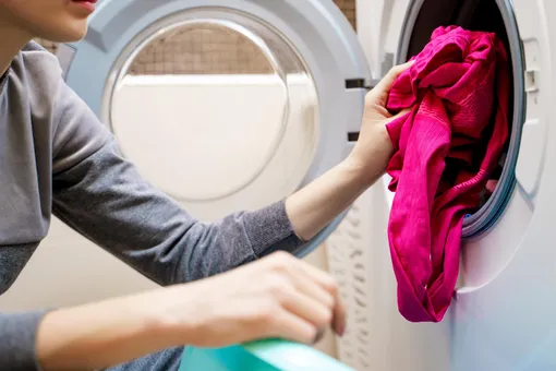 Девушка сует белье в стиральную машину