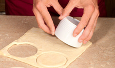 Разогрейте духовку до 200°С. Слоеное тесто тонко раскатайте. Выемкой сделайте круглые лепешки из теста.