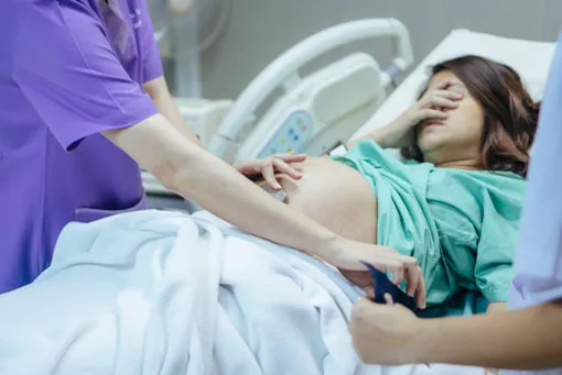 беременная лежит на кровати, закрыв лицо рукой, врач слушает ее живот