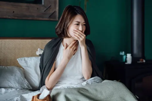 беременная женщина сидит в кровати, закрывая рот рукой