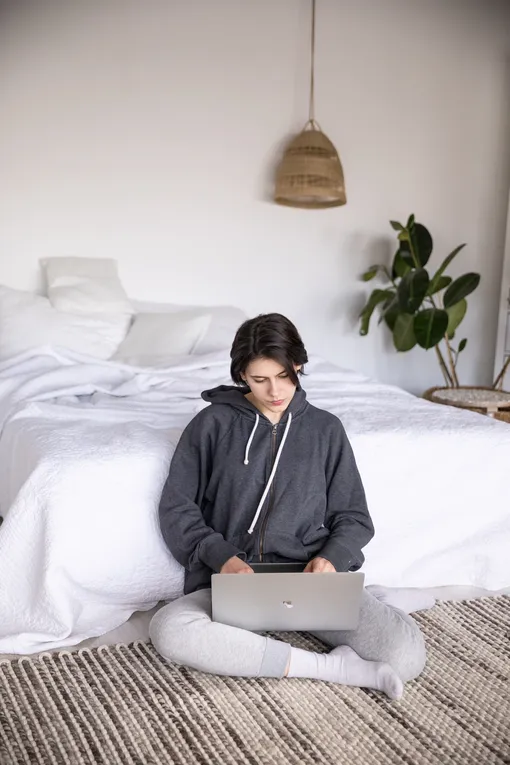 Девушка сидит на полу в спальне и печатает на ноутбуке, отношения на расстоянии