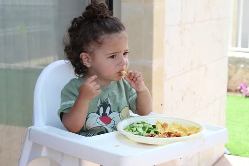 маленькая девочка перед тарелкой с едой с недовольным видом
