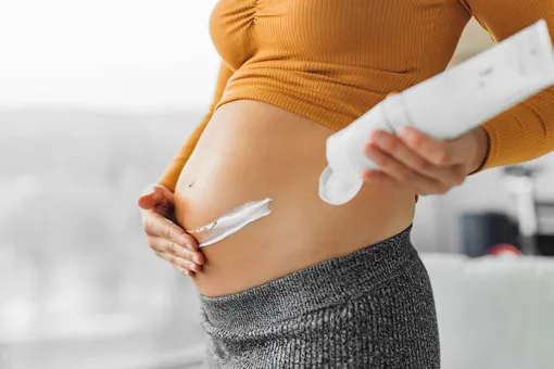 Беременная женщина мажет кремом живот