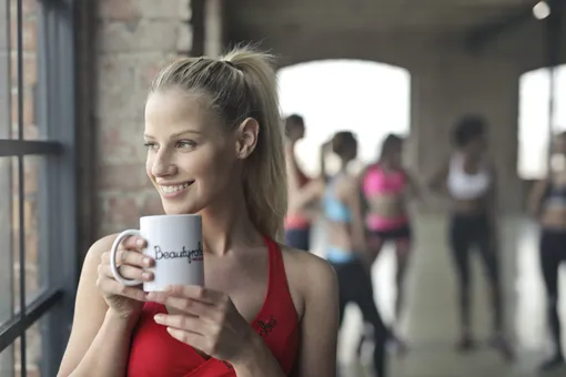 Девушка в спортзале пьёт кофе